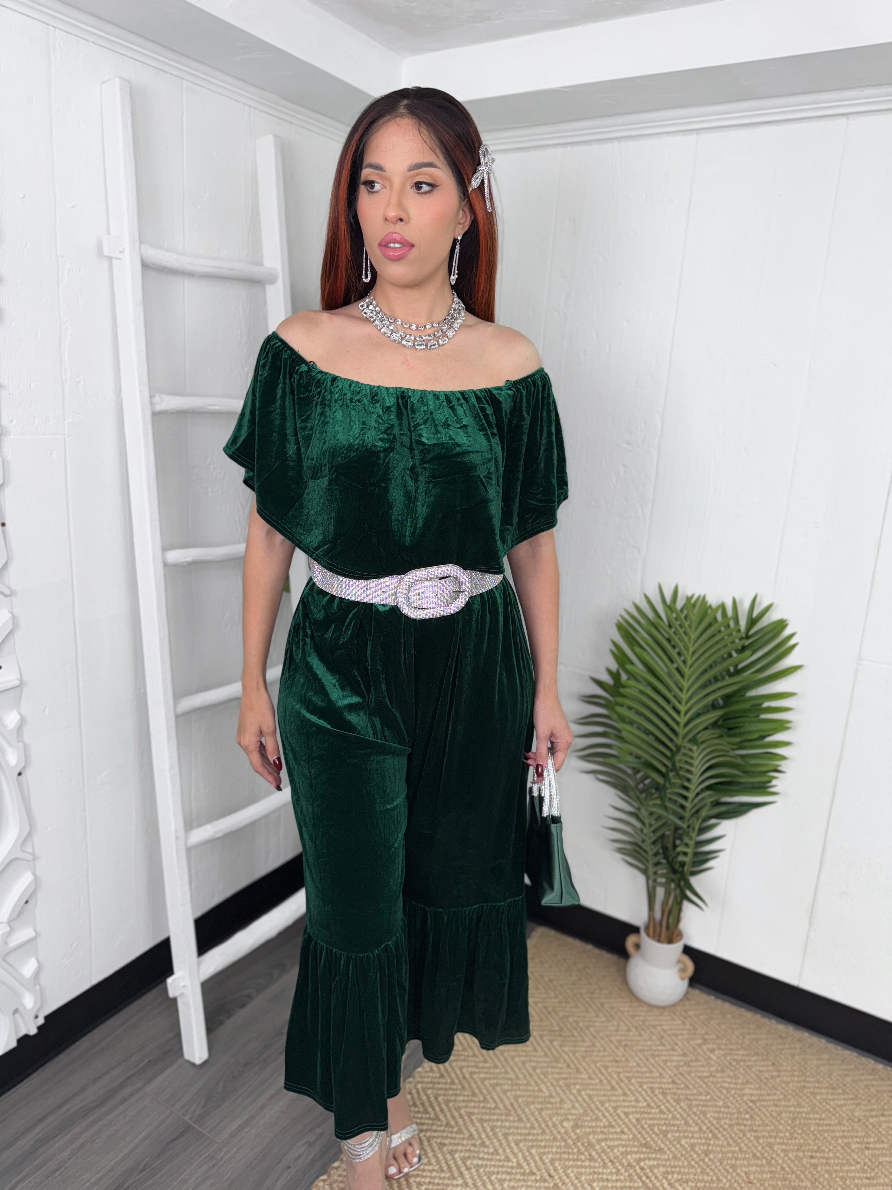 Woman wearing green velvet off-shoulder jumpsuit with silver belt for festive occasions